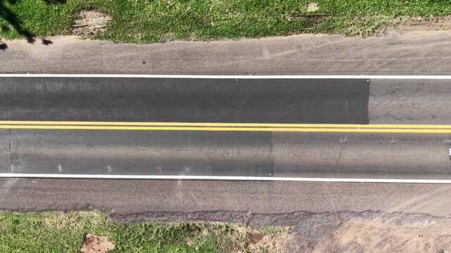 Aerial view of a road with visible lanes. The road has a center yellow line separating two black lane and also two white lines in both sides