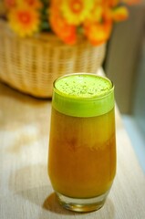 Refreshing beverage: orange juice topped with green matcha foam in a tall glass, bright setup.