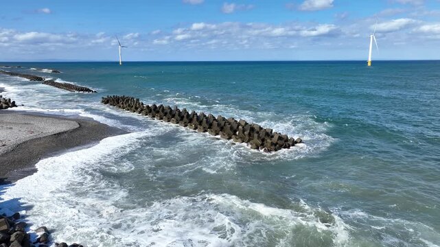 冬が近く風の強い富山湾沿岸の洋上風力発電風車や波のかかる離岸堤などの風景