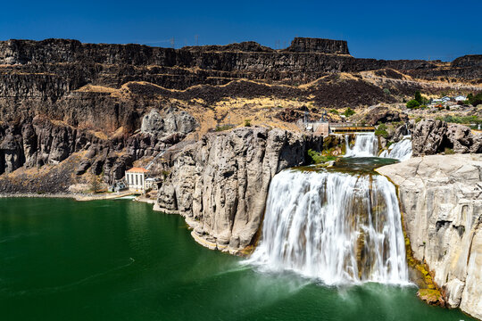The powerful Shoshone Falls, the Niagara of the West, cascades into the green Snake River in Idaho. The waterfall flows over high basalt cliffs under a clear, deep blue sky on a sunny day - Powered by Adobe