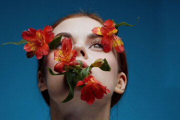 Young woman with flowers on her face, exuding calmness and beauty against a blue background,...