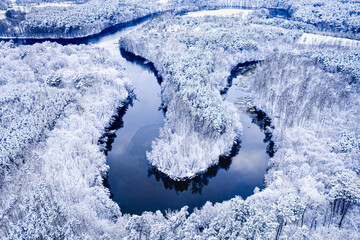 Winter winding river and snowy forest. Aerial view of Poland