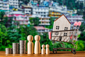 Small wooden toy house in shopping cart, stack of coins and figures of people on nature background. Concept of save money for purchase or construction of home, mortgage and real estate investment