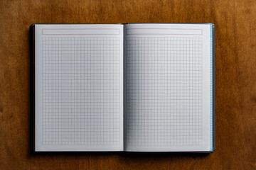 Open notebook with checkered sheets on wooden texture background, closeup, top view, copy space