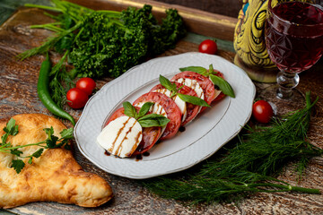 A colorful platter showcases delicious Georgian food, featuring sliced tomatoes, creamy cheese, and fresh herbs. The rustic ambiance is enhanced by surrounding greens and a glass of wine