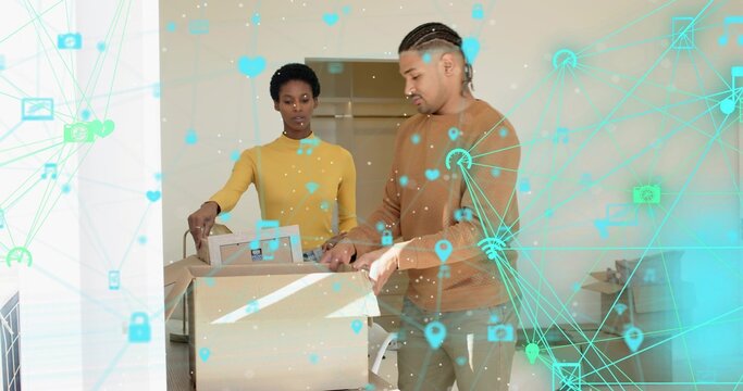 Unpacking couple in mustard top tan sweater standing over large moving box at home, tablet visible - Powered by Adobe