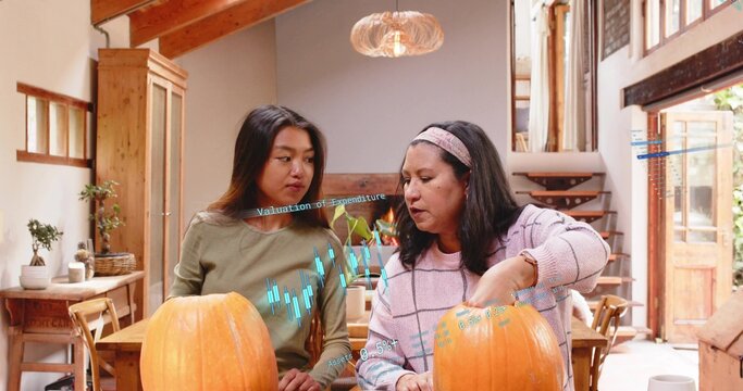 Carving women in olive top and pink sweater working on pumpkins in loft home, charts overlay