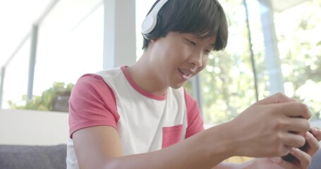 Leaning man wearing red-and-white raglan shirt and white headphones holding smartphone by windows