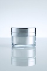 Obraz premium Clear glass jar with silver lid, showcasing cream on smooth surface under soft lighting