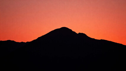 Fototapeta premium Silhouette of a mountain range against a vibrant orange and red sunset sky