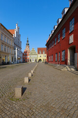 Obraz premium Cobbled market square in Greifswald, Germany, featuring the ornate historic town hall, colorful building facades, and bright blue sky. A classic scene of architecture, travel, and cultural heritage.