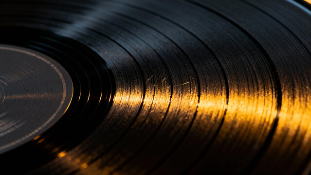 Close-up of a vinyl record with golden light reflecting off its grooves - Powered by Adobe