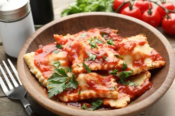 Delicious ravioli with tomato sauce and parsley served on wooden table, closeup