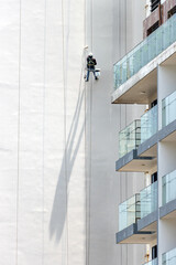 A professional worker paints the tall exterior wall of a building with his shadow on a facade