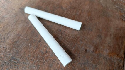Two white chalk sticks on a rustic wooden table with natural texture. This simple yet meaningful image represents education, learning, and creativity. Perfect for school-themed designs, educational co