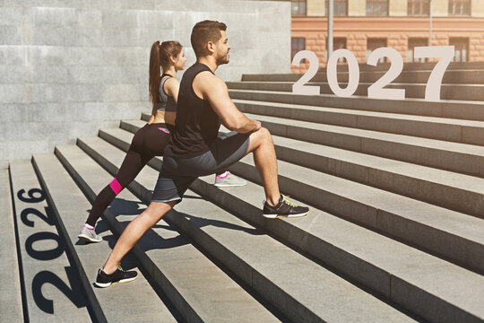 Two fitness enthusiasts perform stretches on a set of stairs while the years 2026 and 2027 are displayed prominently. This scene captures dedication to health and future goals.