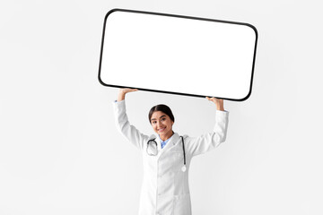 A happy young Hindu female in a white coat raises a large smartphone with a blank screen above her...