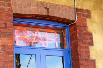 Red neon bar sign above blue door and brick and limestone building.