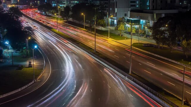 Vista a&eacute;rea de una autopista urbana de noche con estelas de luz de veh&iacute;culos en movimiento, creando un efecto din&aacute;mico y vibrante.