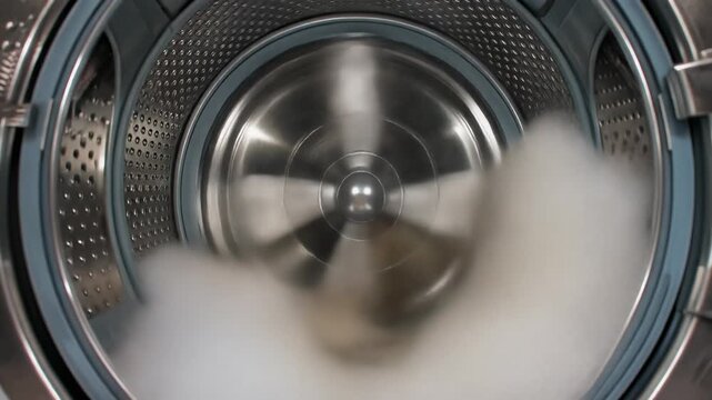 Interior de una lavadora moderna con el tambor girando y ropa blanca en movimiento.