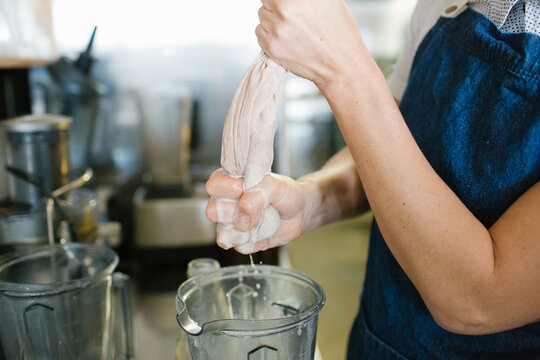 Cafe crew wearing denim apron squeezing a white cloth over container