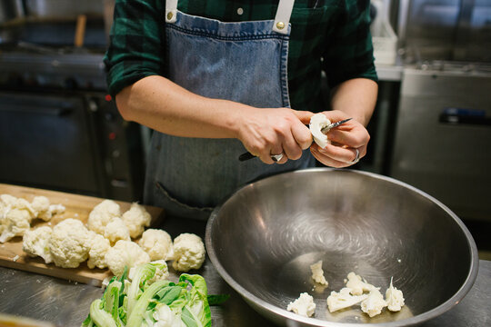 Hands slicing cauliflower in kitchen over metal bowl