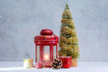 Red lantern with burning candle, miniature Christmas tree, pine cone and gift boxes on snowy background. Concept for Christmas and New Year themes.