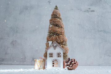 Cozy winter holiday composition featuring small decorative house, a Christmas tree, a drum ornament, and a pine cone covered with snow. Concept for greeting cards and Christmas and New Year projects.