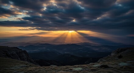 Dramatic sunset with sunbeams breaking through dark clouds over mountains