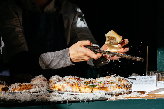 Parmesan Cheese in Hand Being Grated Over Pizza at Restaurant
