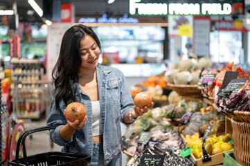Asian woman holding shopping basket while looking or buying onions at vegetables zone in supermarket