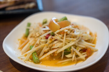 A Thai papaya salad on a plate, shredded green papaya, tomatoes, peanuts, and lime, placed on a table