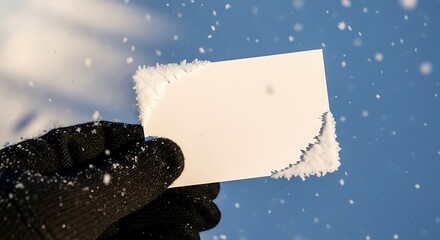 Hand in glove holding snowy card against winter sky.