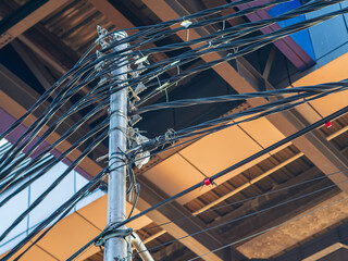 Naklejka premium Close-up view of electric utility pole with tangled overhead cables and wires against modern building background, symbolizing urban infrastructure and power distribution.
