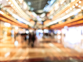 Abstract blurred image of a shopping mall interior with bright lights and people walking, representing retail lifestyle, consumerism, and modern urban atmosphere.