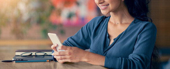 A young woman is sitting at a wooden table in a coffee shop. She is smiling as she checks her...