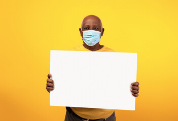 A senior black man wears an anti-COVID face mask while holding a blank advertisement board in a bright orange studio. He is promoting a service with a clear message.