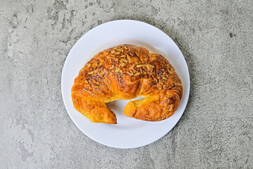 Top view of one cheese croissant on white plate. close up. grey or gray cement on the background. High angle, above, flat lay.
