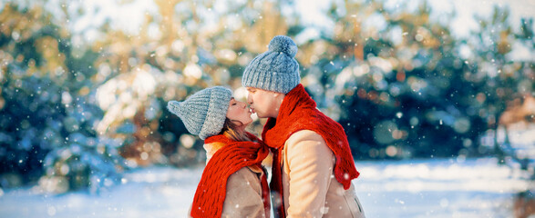 A couple stands close in the snow, smiling and sharing a joyful moment. They embrace each other, wearing warm hats and red scarves, surrounded by a serene winter landscape.
