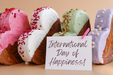 Holiday celebration INTERNATIONAL DAY OF HAPPINESS caption on greeting card Heart shaped different variety flavor croissants on beige background with copy space. Puff pastry new trendy sweet dessert