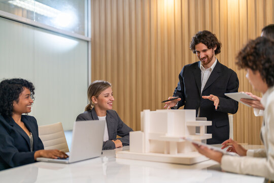 Architects engineers collaborating on building design project in modern office, diverse team of professionals female muslim architect and male engineers discussing architectural model of structure