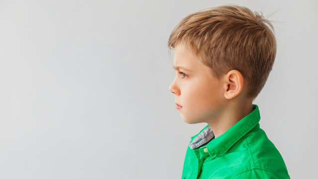 Blonde preteen boy poses in profile against a smooth gray background. He is looking aside with a thoughtful expression, wearing a green shirt. This setting provides room for text and advertisement.