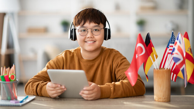 A positive overweight Chinese teenager, wearing a wireless headset, studies foreign languages using a digital tablet.