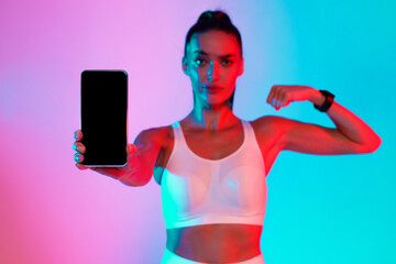 A fit woman stands in a colorful space with bright blue and pink lights. She holds a smartphone...