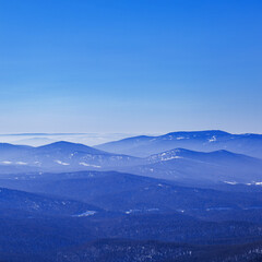 Aerial view of mountain ridges in soft fog. Beautiful white blue Peaks fades into distance. Minimal Nature abstract landscape, natural gradient color, environment winter serenity, panoramic skyline.