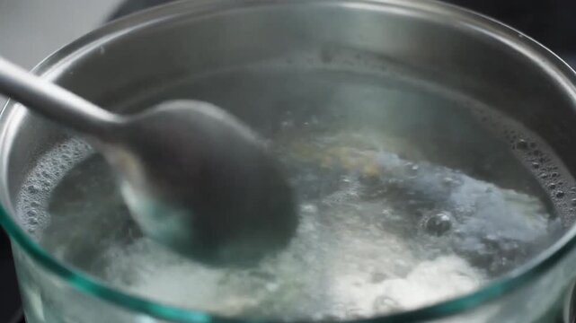 Stirring Boiling Water in a Glass Pot with a Spoon.