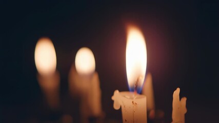 Close-up of lit candles with a sharp focus on one flame, surrounded by a dark, blurred background