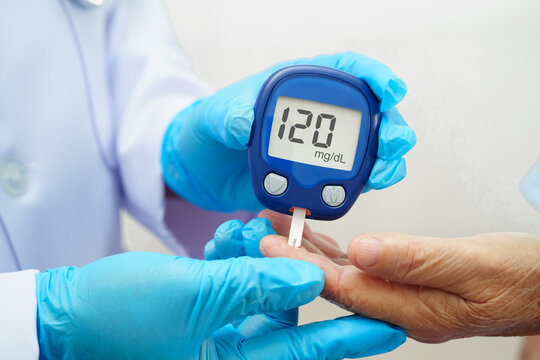Asian doctor using digital glucose meter for check sample blood sugar level to treatment diabetes.