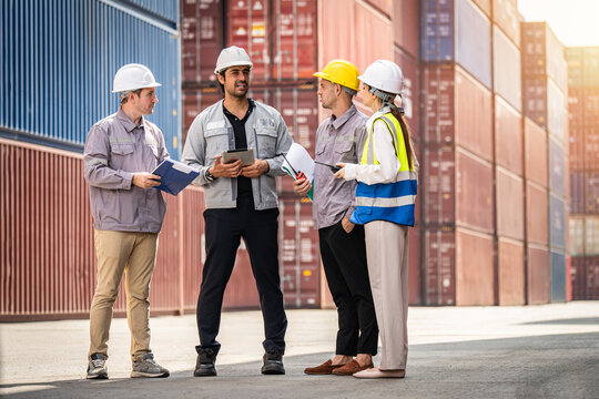 A group of construction workers are standing in front of a large container. They are wearing hard hats and holding papers