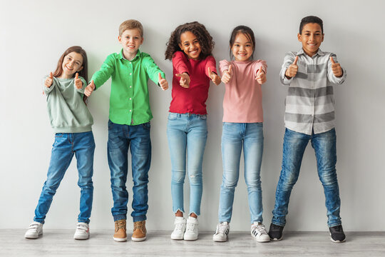 A group of happy, diverse children pose indoors, standing close together and giving thumbs up. They are smiling and seem to enjoy their time as they celebrate their friendship.